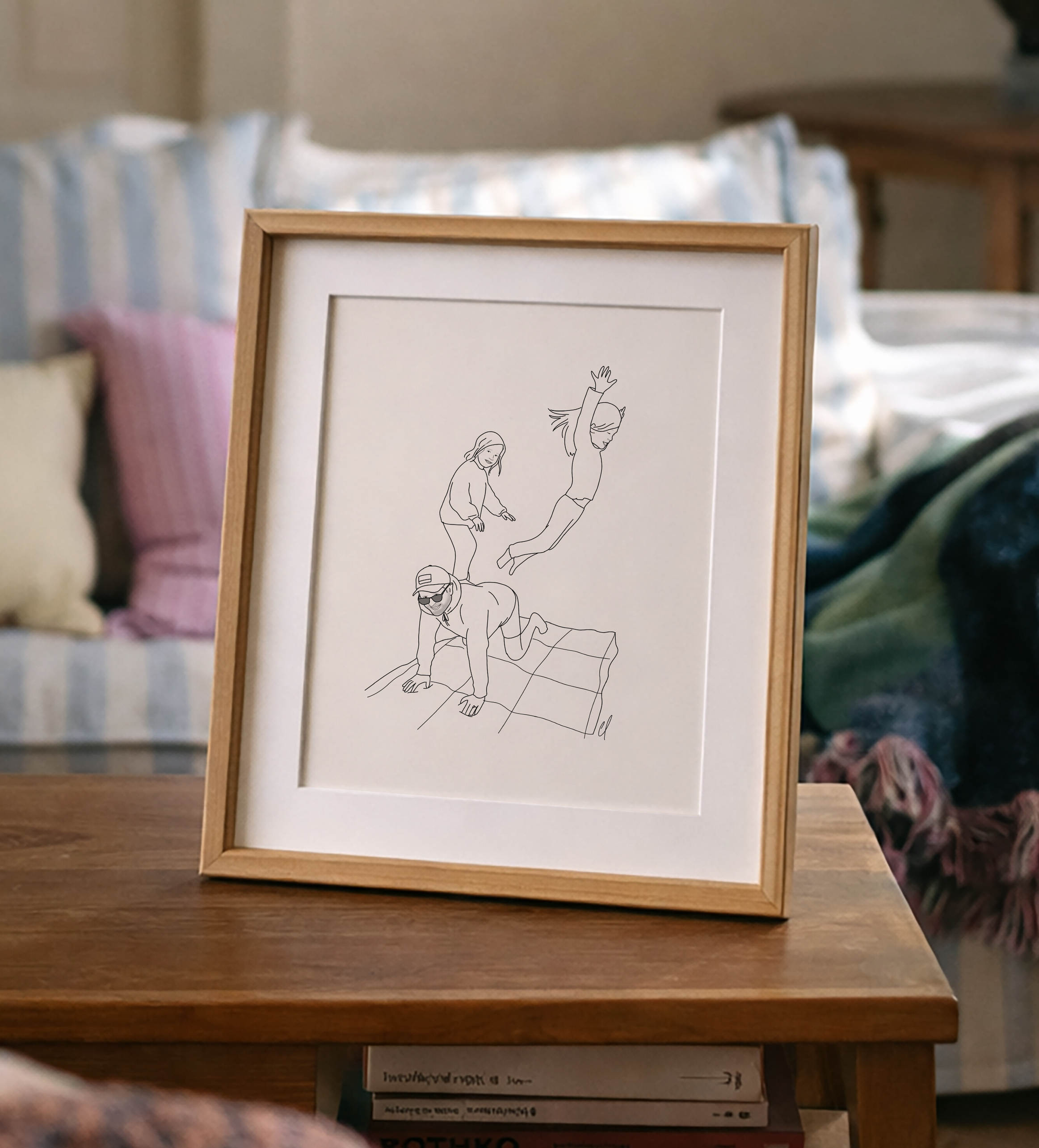 Framed line drawing of a person and dog on a wooden table with a cozy living room background.